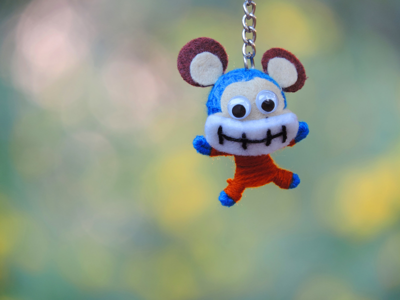 A small plush toy resembling a cartoonish mouse character is hanging from a metal chain against a blurred outdoor background with soft green and yellow tones. The toy...
<br/>
<a class=